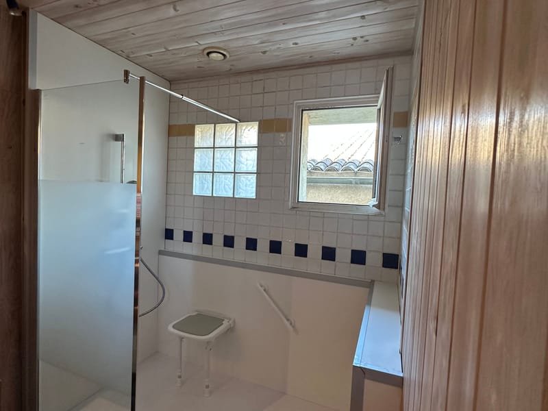 Douche de plain-pied avec paroi vitrée, siège rabattable et barre d'appui